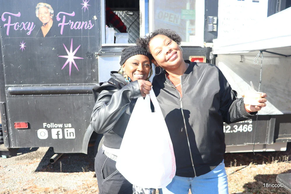 Two happy customers posing with their order in front of the Foxy Fran's food truck
